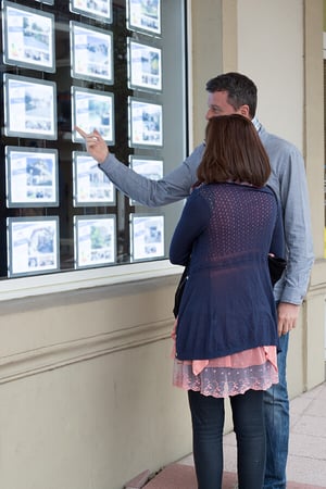 deux-personnes-femme-homme-regardent-annonces-immobilieres-vitrine-agence